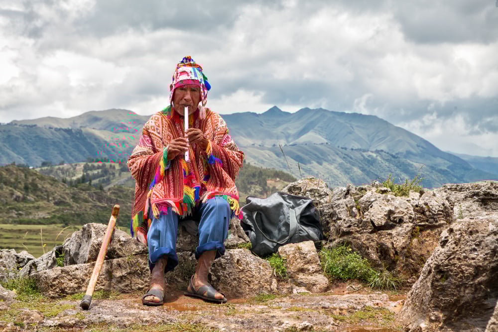 Elderly Quechua man in a bright poncho playing a flute in Cusco